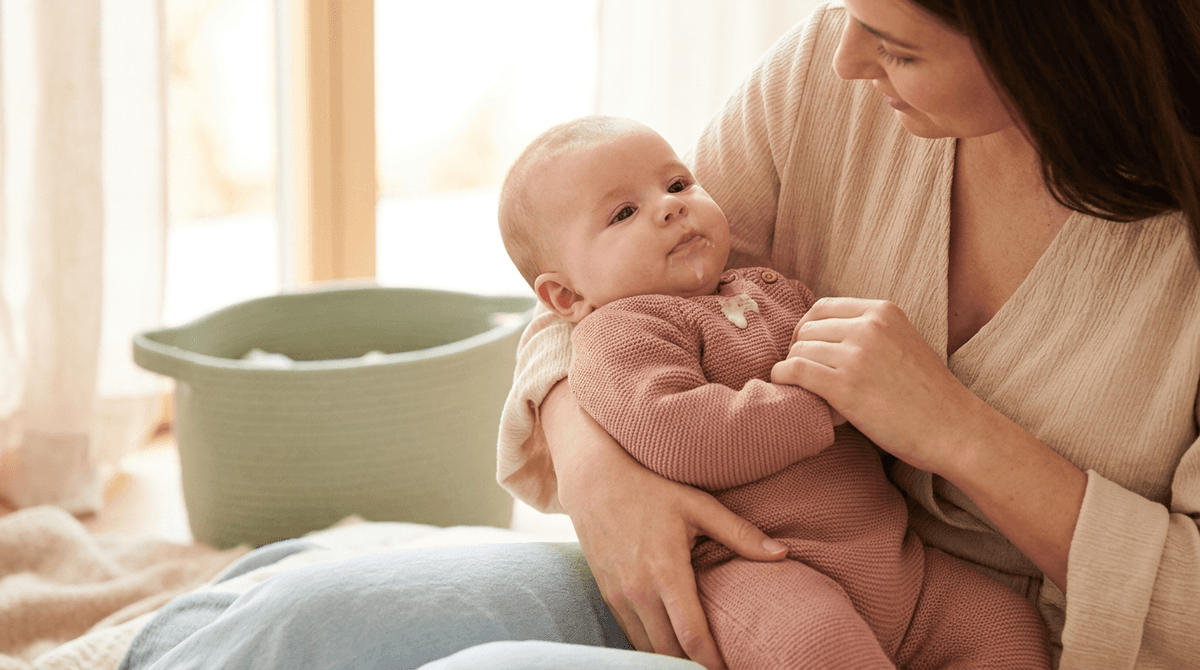 Mère tenant son bébé calmement, avec une légère régurgitation, dans une ambiance douce et pastel.